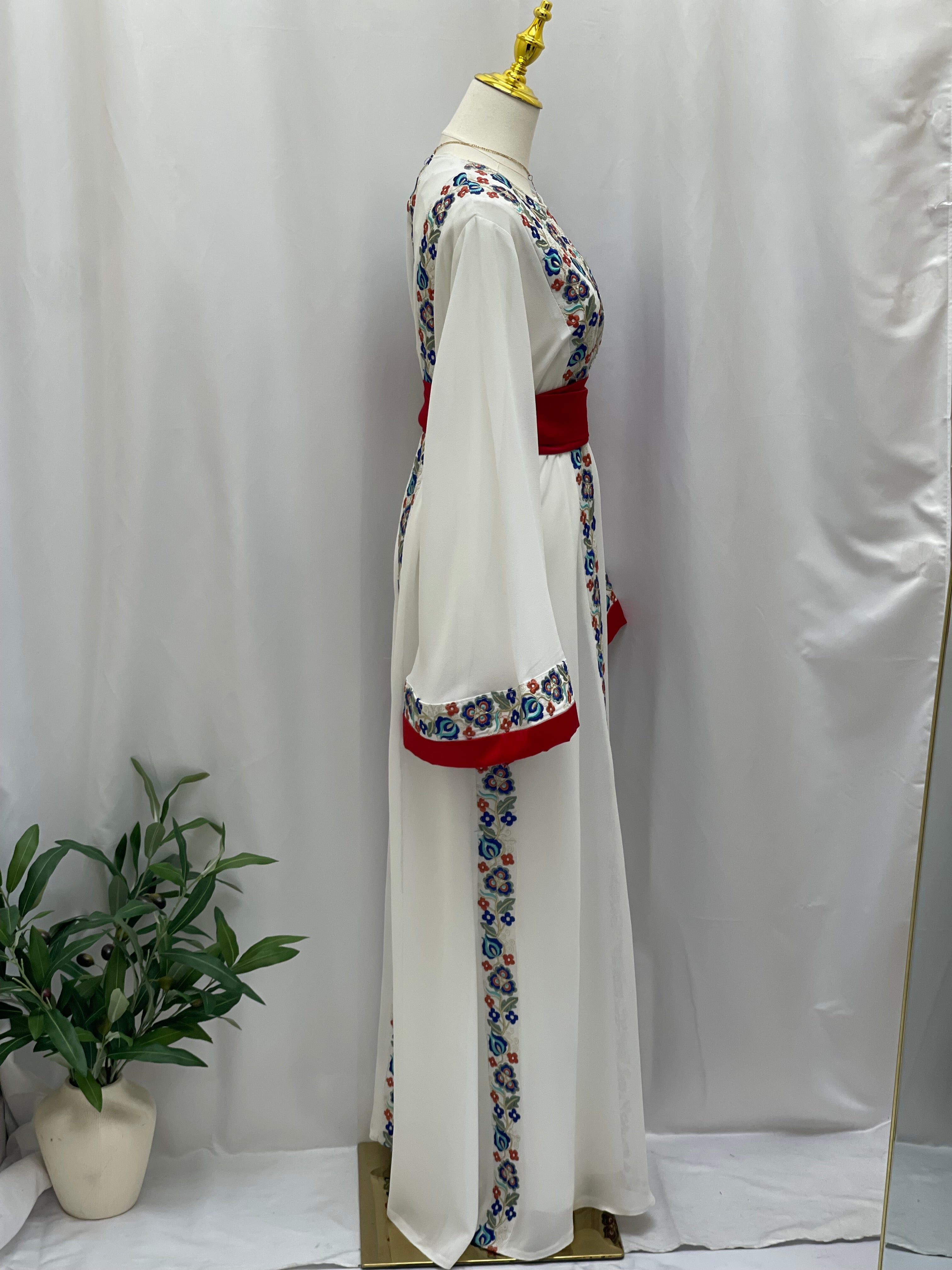 White Palestinian embroidered dress with floral embroidery and red accents displayed on a mannequin