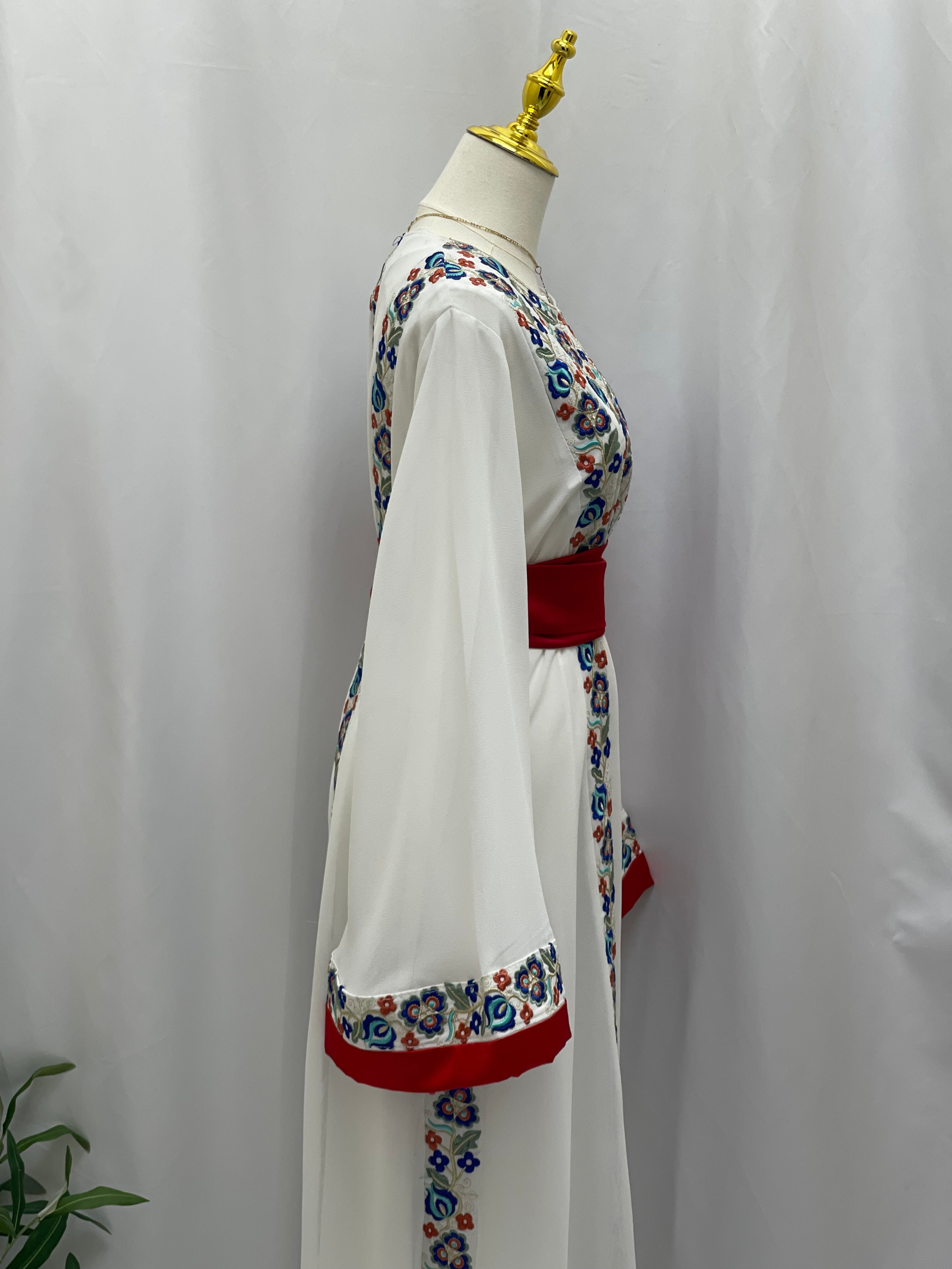 Side view of a white Palestinian embroidered dress with multicolor floral patterns and red sash by Palestinian Elegance