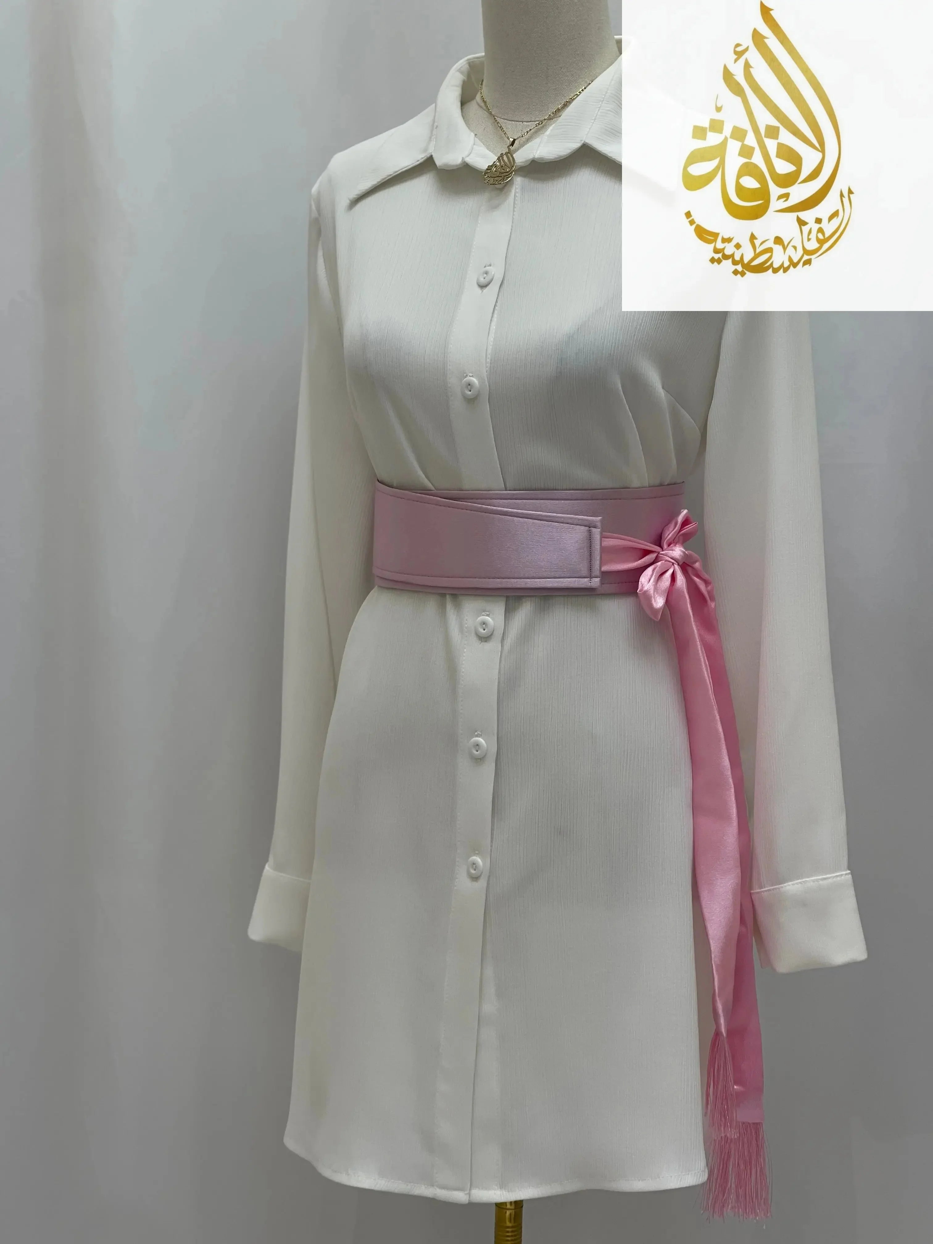 Pink satin belt for dresses tied in a bow over a white button-down dress on mannequin