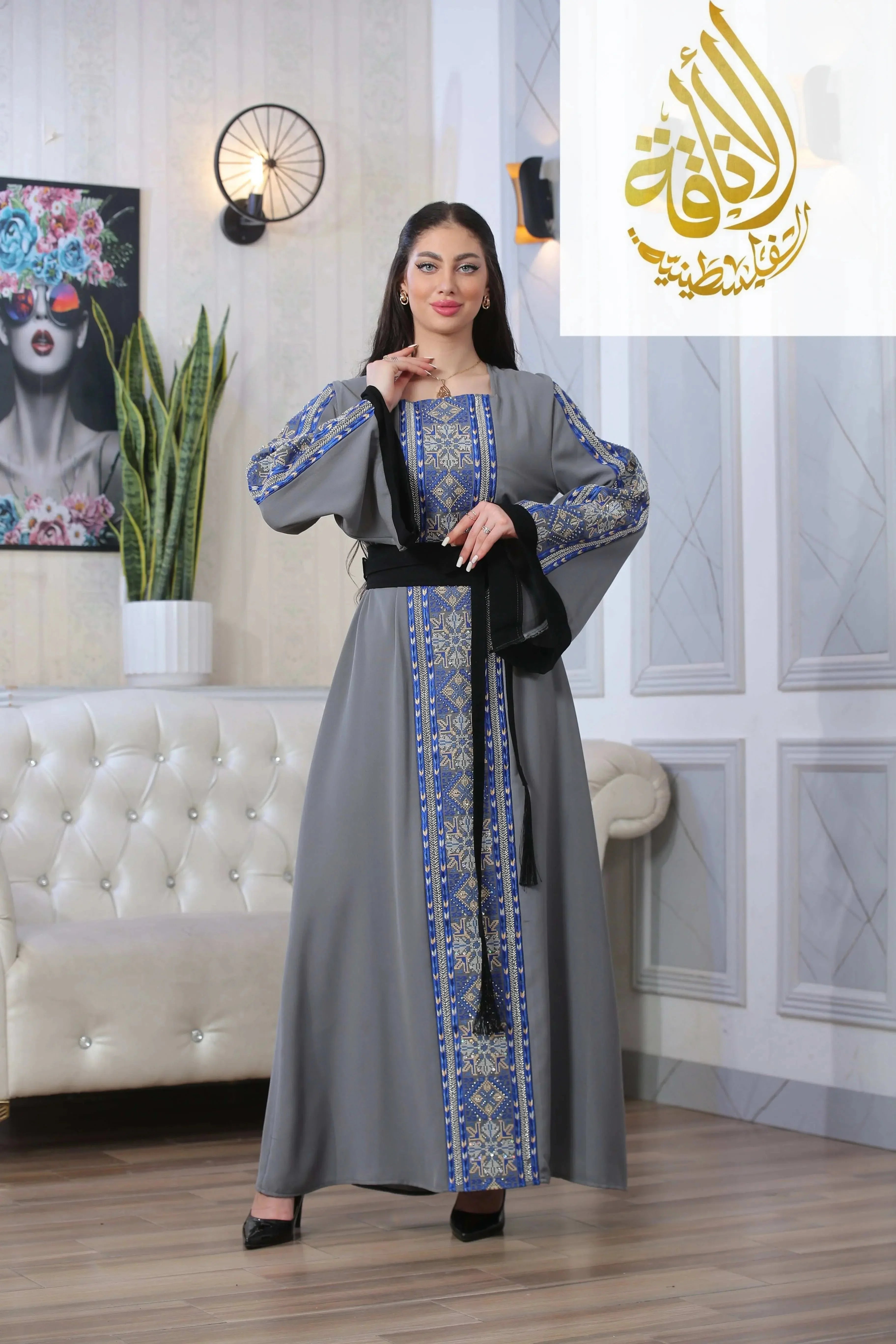 Palestinian Elegance woman wearing Moroccan Rana Jalabia Thoub with blue embroidery and black belt indoors