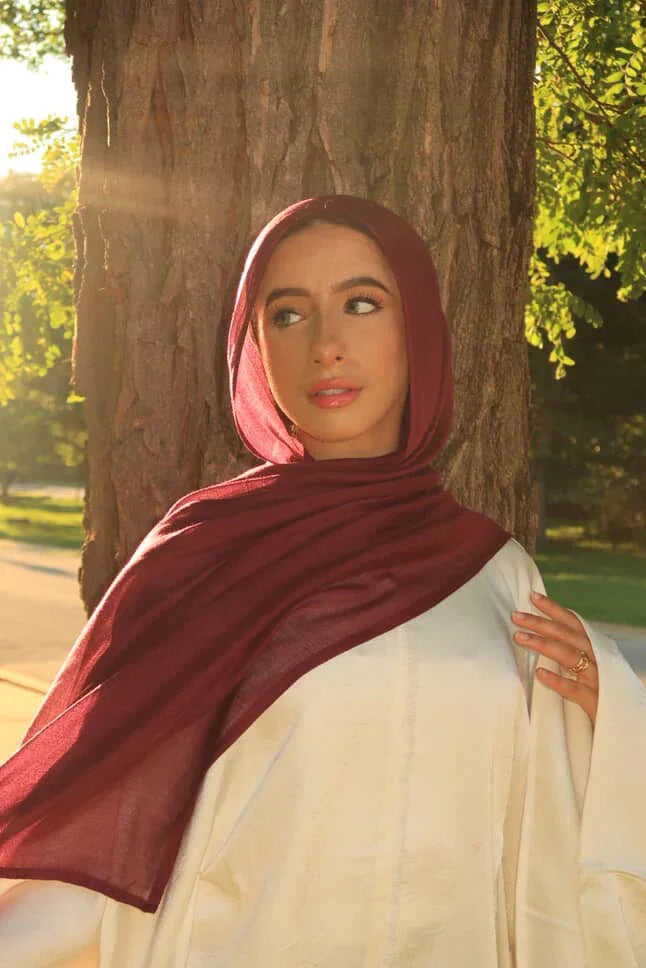 New Modal Hijab burgundy lightweight drape on model leaning against tree in warm sunlight Palestinian Elegance