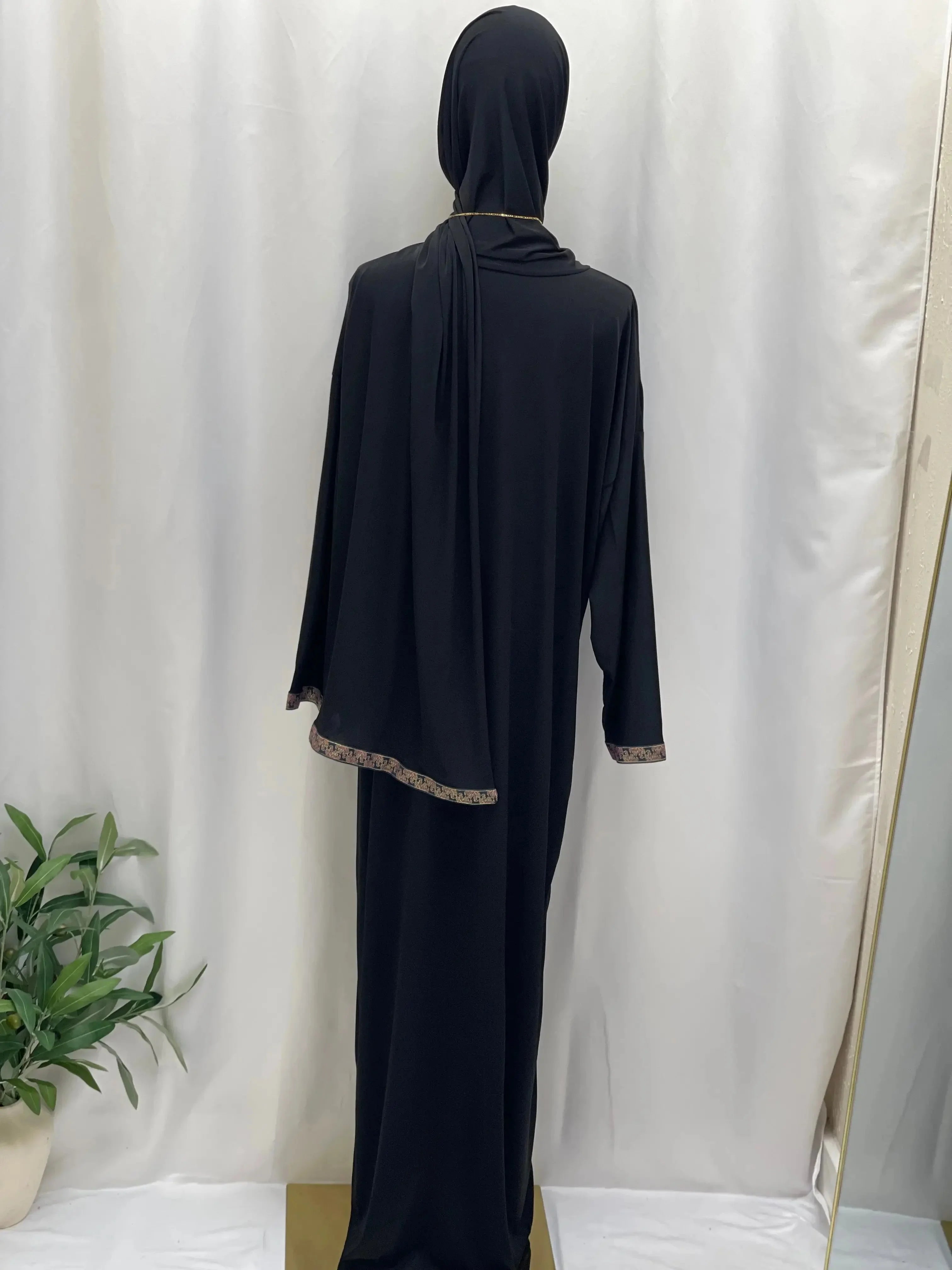 Black one piece prayer dress abaya by Palestinian Elegance with gold trim detailed hems