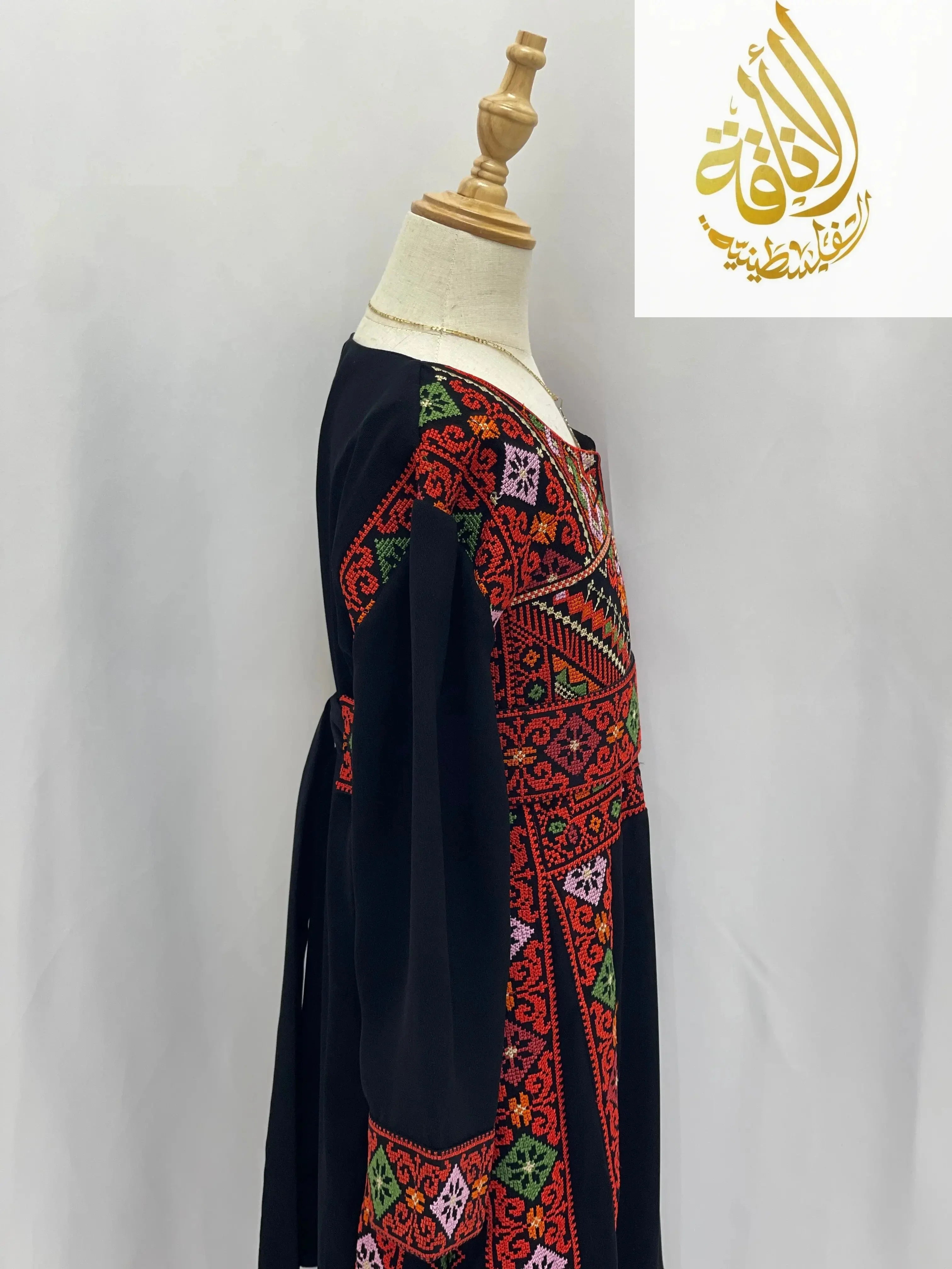 Embroidered thoub for girls from Palestinian Elegance featuring vibrant traditional red and green patterns on black fabric