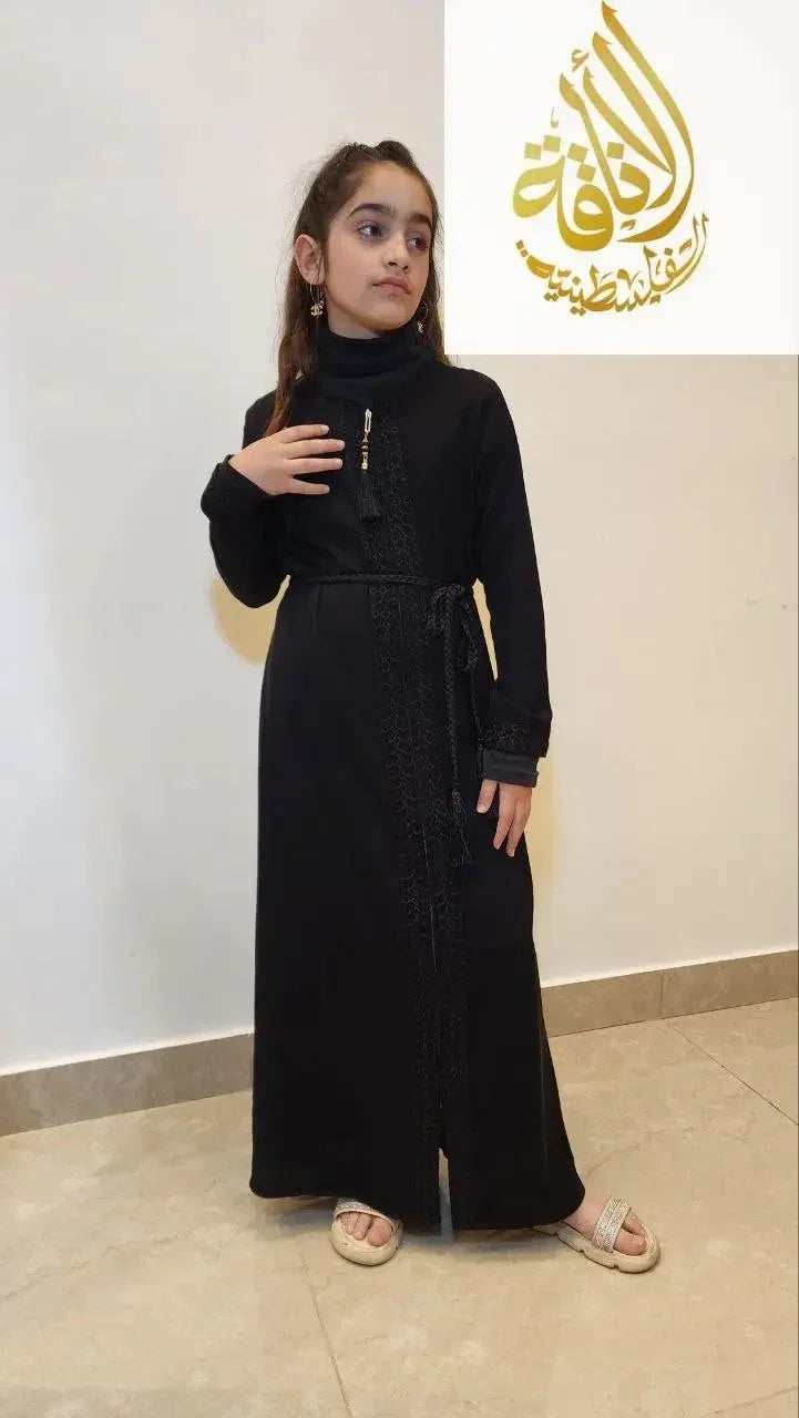 Girls black abaya dress by Palestinian Elegance with embroidered details and a waist belt on a young girl
