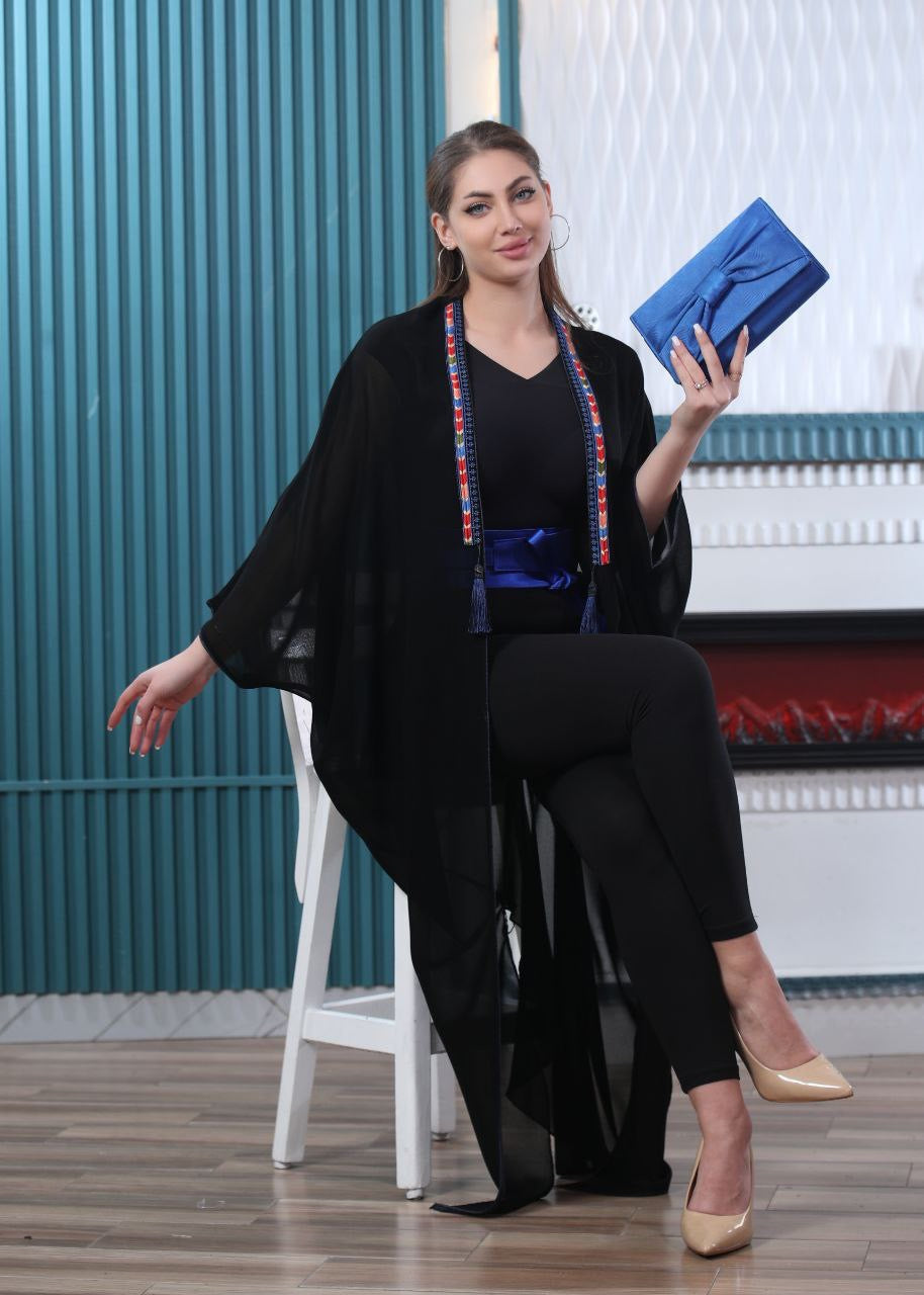 Palestinian Elegance embroidered chiffon cardigan worn by woman holding blue clutch sitting on white chair