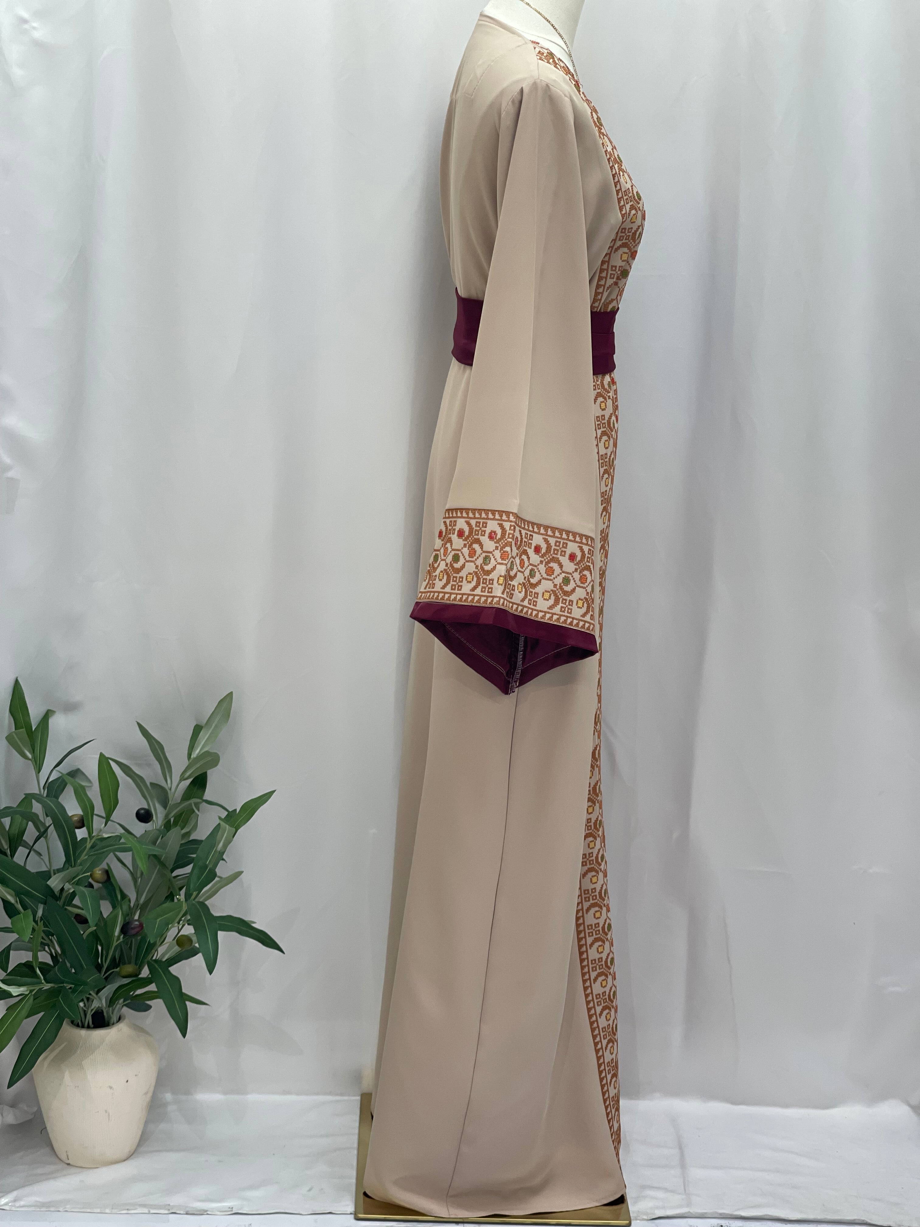 Palestinian Elegance Embroiderd Thobe With Belt in beige with intricate embroidery and maroon belt on mannequin