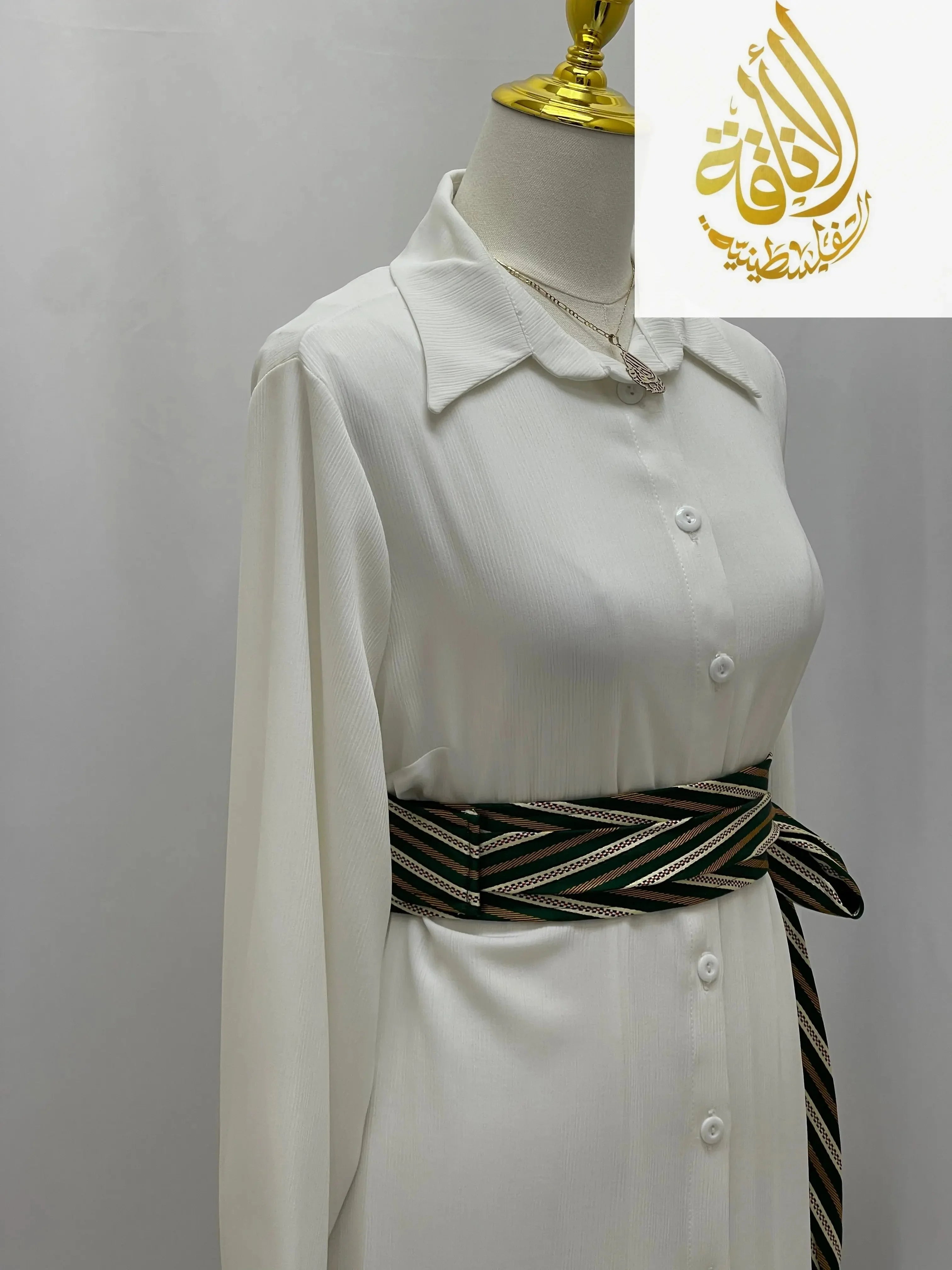 Palestinian embroidered belt with geometric patterns worn over a white long sleeve dress