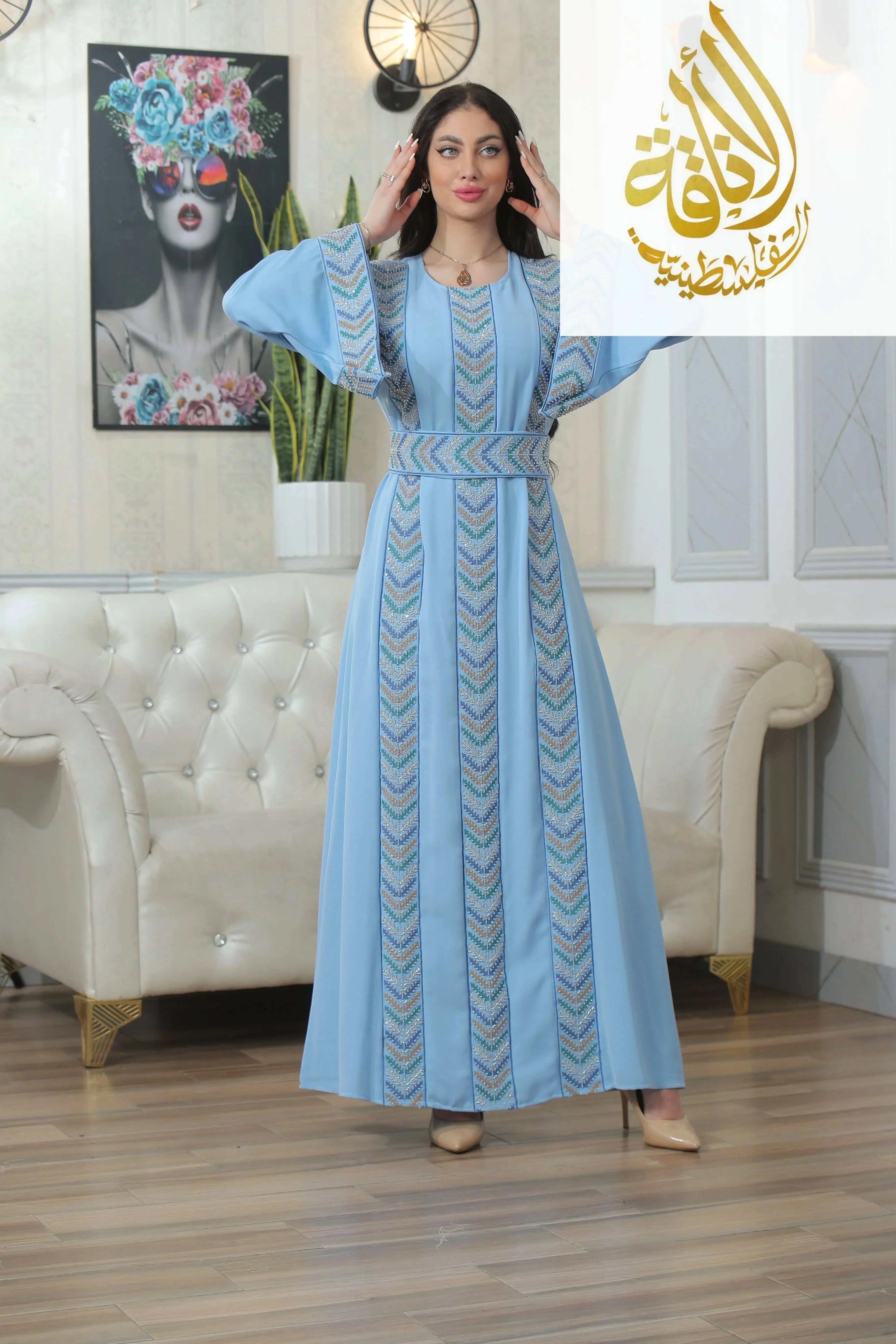 Woman wearing a light blue Seham Embroidered Beads Thoub by Palestinian Elegance in a stylish living room