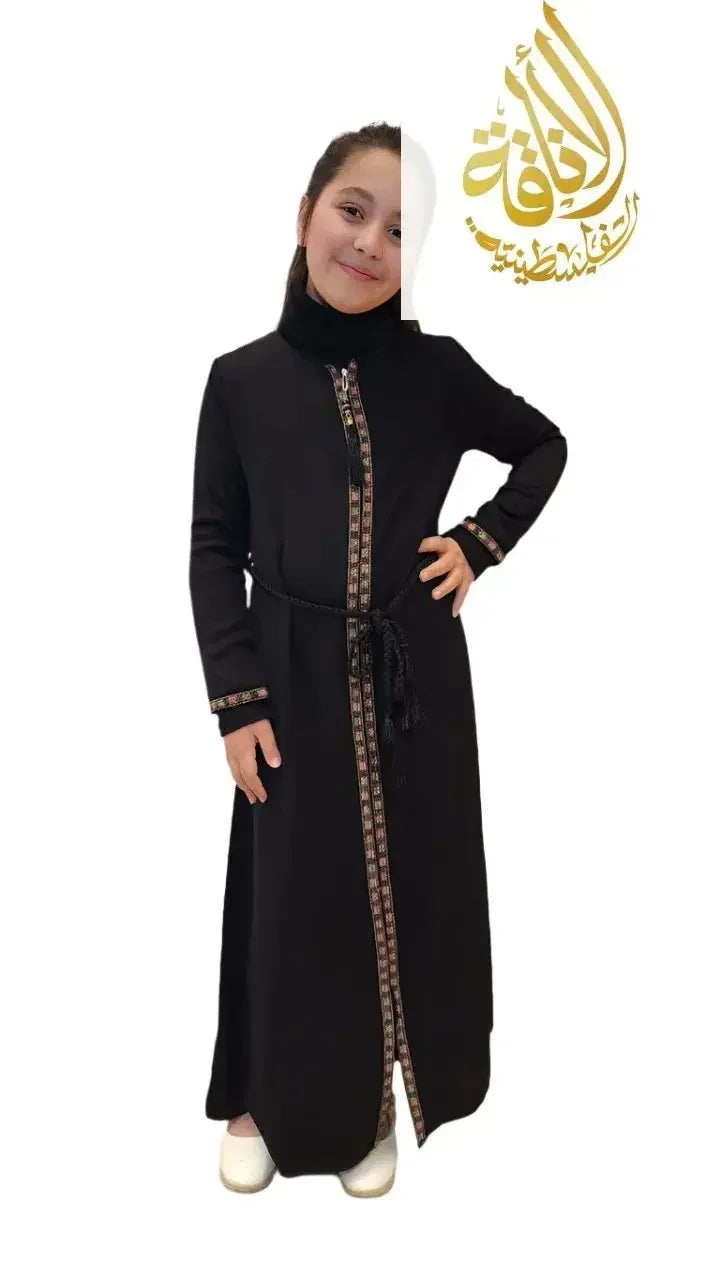 Girl wearing a black embroidered abaya for girls with decorative trim and a belt from Palestinian Elegance